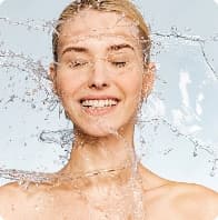 Ženska s sijočo kožo, ki uživa v brizganju vode, predstavlja vlažilno nego kože.